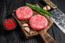 Raw Steak Cutlets With Mince Beef Meat And Rosemary On A Wooden Cutting Board With Meat Cleaver. Black Wooden Background. Top View