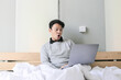 © Reezky - Surprised and shocked Asian man is working with his laptop on his cozy bed. Concept of successful freelancer lifestyle.