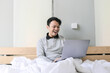 © Reezky - Surprised and shocked Asian man is working with his laptop on his cozy bed. Concept of successful freelancer lifestyle.