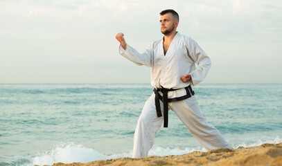 Glad guy practising karate kata poses at seaside