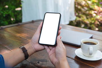 Mockup image of a woman holding mobile phone with blank white desktop screen with coffee cup on the table