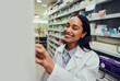 © StratfordProductions - Cheerful female pharmacist wearing labcoat searching for medicine in shelf in chemist