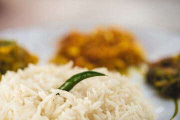 Indian Homemade Bengali Style Food. Indian veg thali or typical home cooked bengali meal background. Closeup shot of a plate full of steam rice with a green chilli. Concept for regional food, lunch.