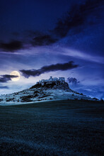 Castle On The Hill At Night. Composite Fantasy Landscape. Grassy Meadow In The Foreground. Rocky Peaks Of The Ridge In The Distant Background In Full Moon Light