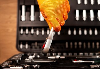 Wall Mural - Male hand in building glove with socket ratchet handle taking from repair suitcase. Industrial metal tool, close up.