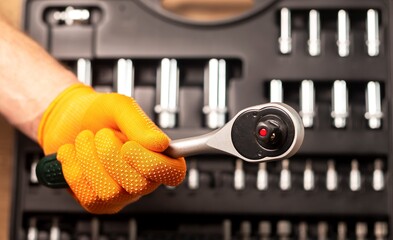 Wall Mural - Male hand in building glove with socket ratchet handle taking from repair suitcase. Industrial metal tool, close up.