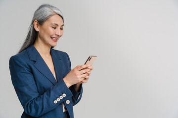 asian mature woman in jacket smiling while using mobile phone