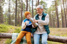 Picking Season, Leisure And People Concept - Grandmother And Grandson Having Picnic And Drinking Tea In Autumn Forest