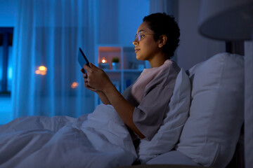 Wall Mural - technology, internet and people concept - young african american woman with tablet pc computer lying in bed at home at night