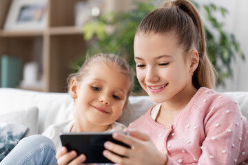 Wall Mural - family, childhood and technology concept - two happy smiling little girls or sisters with smartphone at home