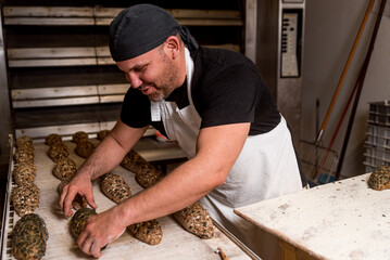 young baker preparing raw bread knead before cooking with a smile in bread shop. concept of artisan bread preparation in bread factory