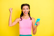 © deagreez - Photo of celebrating young lady braids dressed singlet rising fist holding modern gadget isolated yellow color background