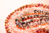 Fototapeta  - Faceted and smooth round beads made of quartz and natural stone on threads on a pink background