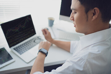 Poster - Young man trades stocks on a laptop screen. He was looking at the watch on his wrist.