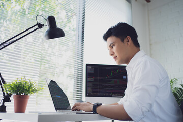 Poster - Young Asian man trades stocks on his laptop screen on his desk. He is serious about trading stocks.