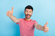 © deagreez - Photo of cute impressed young man dressed striped t-shirt showing two thumbs up isolated blue color background