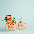 Retro orange bicycle with flowers flying out of basket against pastel green background. Creative flower delivery concept. Florist or spring bloom banner with copy space. Natural romantic card.