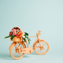 Retro Orange Bicycle With Flowers Flying Out Of Basket Against Pastel Green Background. Creative Flower Delivery Concept. Florist Or Spring Bloom Banner With Copy Space. Natural Romantic Card.