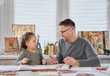 © boytsov - Spending time together concept. Happy attractive caucasian family creative art hobby and funny time spending. Daughter with weird face is surprised teaching father how to draw with crayons