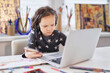 © boytsov - Doing business or small businesswoman concept. Cute small preschool girl in headphones sitting at the table using laptop computer and smartphone for education or homework doing. High quality photo