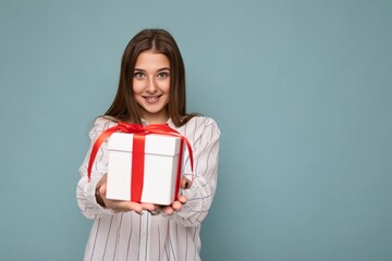 Beautiful happy young dark blonde woman isolated over colourful background wall wearing stylish casual clothes holding gift box and looking at camera