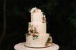 Luxury wedding tiered white cake decorated with flowers, photo at night on the background of lights