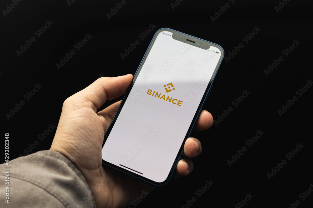 Kharkov, Ukraine - April 20, 2021: Man hold smartphone with Binance crypto app for buying bitcoin and other cryptocurrency, black background with application logo