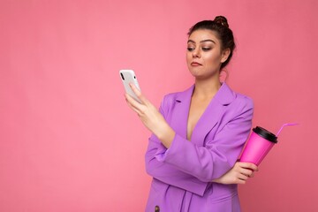 Wall Mural - Young amazed shocked woman isolated over pink background with copy space holding coffee to take away and a mobile phone