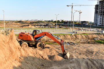 Excavator working at construction site on earthworks. Backhoe on road work and aying sewer pipes. Construction machinery for digs ground, excavating foundation. Tower cranes in action