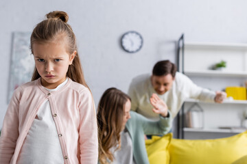 Displeased kid looking at camera while parents quarreling.