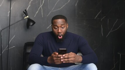 Shocked African-American man holding a smartphone, feel astonishment with a unexpected news, surprised black guy looks at phone screen and does not understand what happened, made a mistake