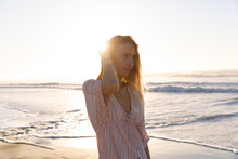Beautiful Caucasian Woman Touching Her Hair Standing At The Beach During Sunset