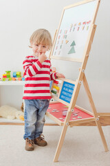 Cute little child playing at a magnetic board, learning letters, numbers and geometric shapes at home. Educative and funny indoor activity for early development.