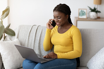 Wall Mural - Smiling Black Woman Talking On Cellphone And Using Laptop Computer At Home