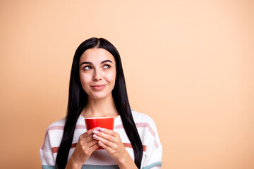 Wall Mural - Photo of young girl happy positive smile dream dreamy look empty space hold cup of tea coffee isolated over beige color background