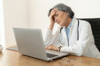 © Vadim Pastuh - Tired stressed senior female doctor in a lab coat sitting in the office in front of a laptop, feeling burnout at work, restless after having no days off or exhausted, and falling asleep
