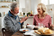 © JustLife - Senior couple eating breakfast in the kitchen. Husband and wife talking and laughing while eating a sandwich...
