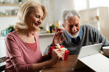 Wall Mural - Senior couple having video call. Happy husband giving his wife a gift..