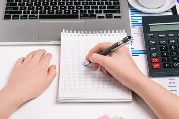 The man writes in a notebook. Workplace with a computer, calculator and financial charts. Preparation of a tax report. Company budget planning. Business and finance concept