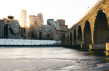 Minneapolis Skyline Next To Sone Arch Bridge With Sun Setting Behind Skyline