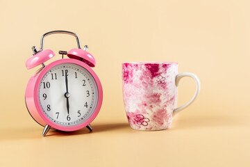 Pink alarm clock and a cup on a beige background. Time Concept. Place for your text.