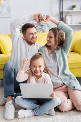 Sticker - Girl with laptop showing yes gesture near smiling parents on blurred background.