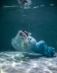 beautiful girl with red hair in a ball gown blue dress underwater on a blue background