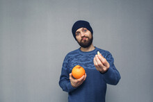 Bearded Guy Holds An Orange And Suppository For Hemorrhoids In His Hands. Hemorrhoids Concept.