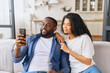 © Vadim Pastuh - African-American couple with smartphone on the couch spends leisure time in social networks, scrolling feed, watching videos, a black guy is showing smth to his girlfriend