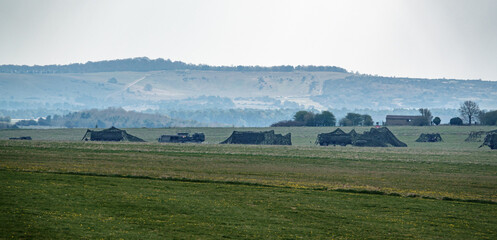 a camp of british army MAN 4x4 logistics vehicles under camouflage netting