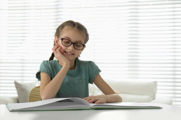 Canvas Print - Cute little girl reading book at desk in room. Space for text