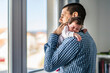 © Miljan Živković - Side view of father holding his newborn baby over the shoulder while standing by the window in day at home - sleepy infant in position for burping new life and parenthood concept