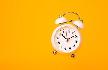 Small white alarm clock, black numbers, set the time placed on a table. Clock on isolated yellow background.