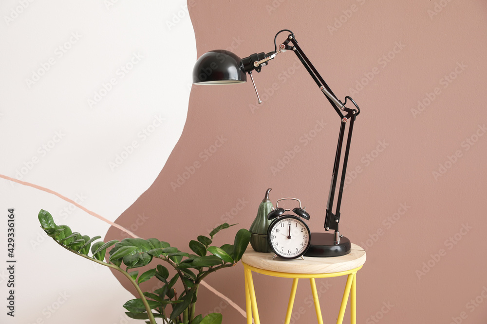 Bedside table with alarm clock and lamp near color wall